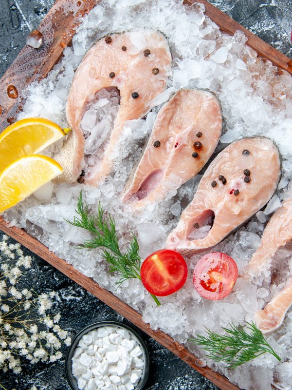 top view raw fish slices with ice on wood board sea salt in small bowl on table